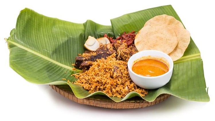 Aromatic delicious nasi briyani meal with mutton and dhal on banana leaf and rattan plate, a popular Indian cuisine