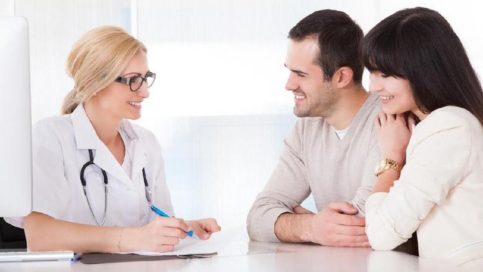 Happy Doctor Discussing With Couple In Clinic