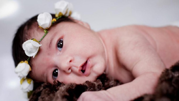 new born baby lie on the bed with flowers crown