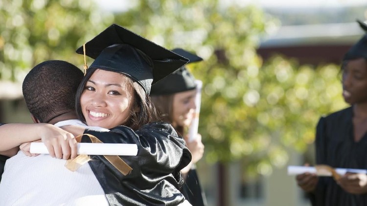 509105528 A happy graduate is hugging her friend after their graduation ceremony. She is smiling while looking at the camera.