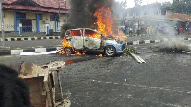 People look on as a car burns during a violent protest in Manokwari, Papua province, Indonesia, Monday, Aug. 19, 2019. The protest was sparked by accusations that Indonesian police who backed by the military, have arrested and insulted dozens of Papuan students in their dormitary in East Java's cities of Surabaya and Malang a day earlier. (AP Photo/Safwan Ashari Raharusun)
