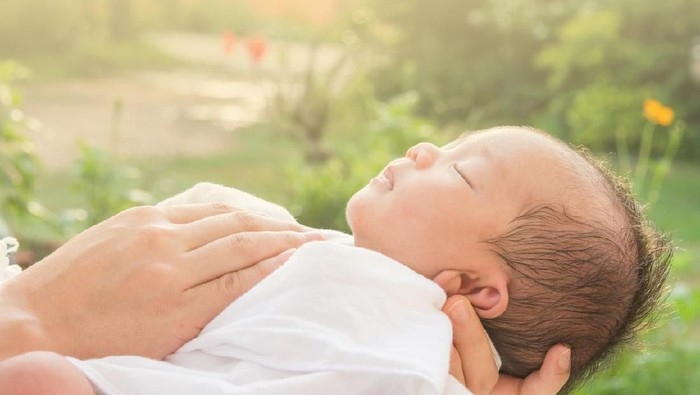 Baby sleeps on mother's hands and morning sun
