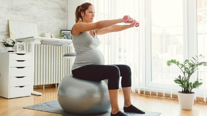 Pregnant woman doing fitness ball and pilates exercise with coach. Happy future mother preparing for childbirth.
