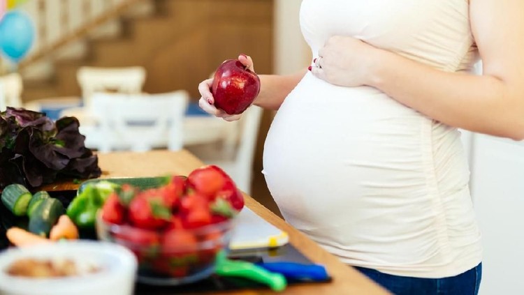 Happy pregnant woman cooking at home, doing fresh green salad, eating many different vegetables during pregnancy, healthy pregnancy concept