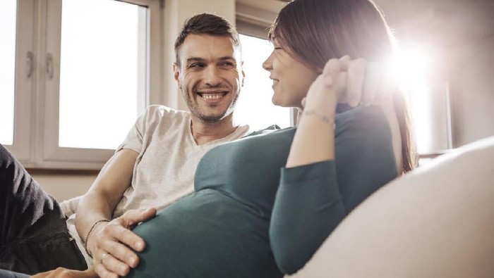 Couple sitting on sofa and relaxing while father touches stomach.