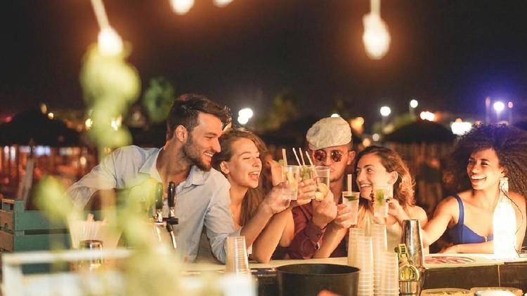 Happy friends cheering and drinking cocktails at beach party outdoor - Young millennials people having fun at weekend summer night - Youth lifestyle and nightlife concept - Main focus on left guys