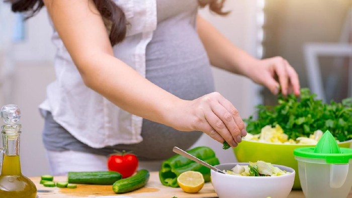 Happy pregnant woman cooking at home, doing fresh green salad, eating many different vegetables during pregnancy, healthy pregnancy concept