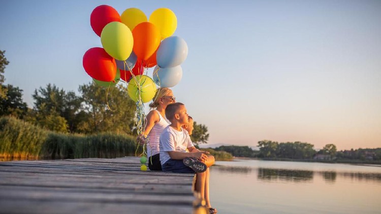 Happy mother and her sons playing with balloons by the lake