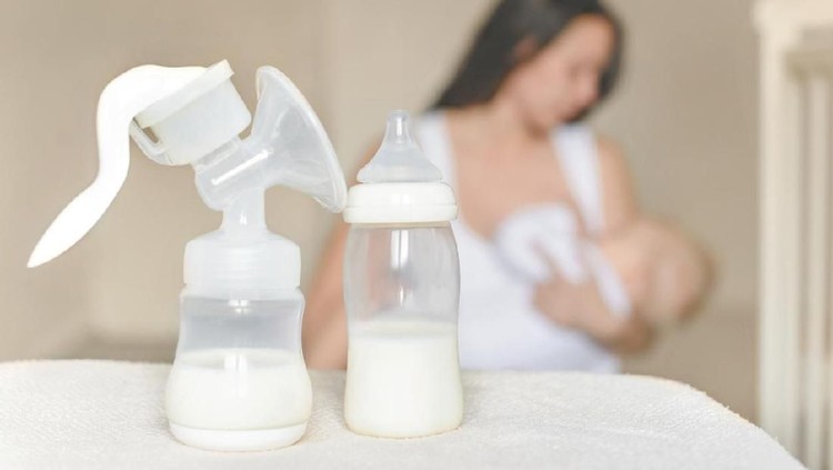 air susu ibu Manual breast pump and bottle with breast milk on the background of mother holding in her hands and breastfeeding baby. Maternity and baby care.