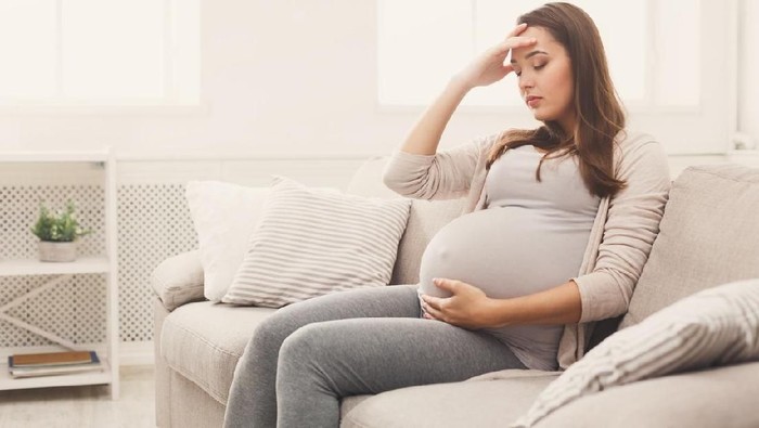 Young pregnant woman with headache sitting on sofa. Pregnancy symptoms, expectation, parenthood concept, copy space