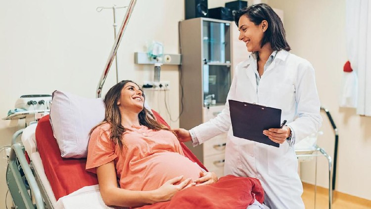 melahirkan Pregnant woman lying down on a hospital bed and talking to a doctor