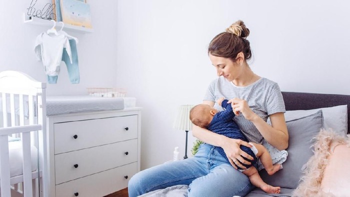 Mother and newborn baby boy are indoors in bedroom. Mother is breastfeeding her son while lying in bed.