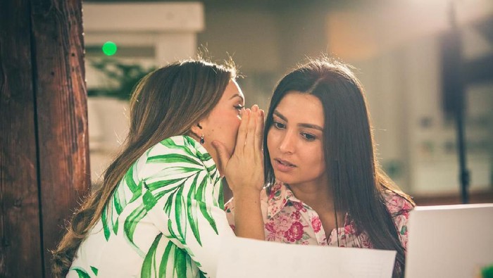 Woman sharing secret with surprised aged mother, daughter whispering in old mum ear, hearing shocking news, family gossiping at home, sitting together on couch, best friends close up