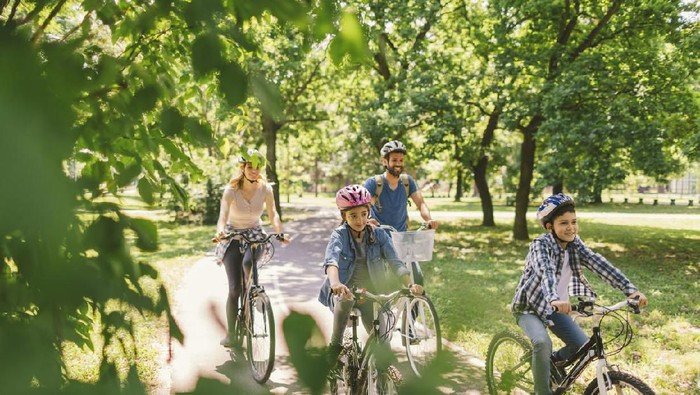 Family riding bicycle in the public park together. Cycling and enjoying the sunny day