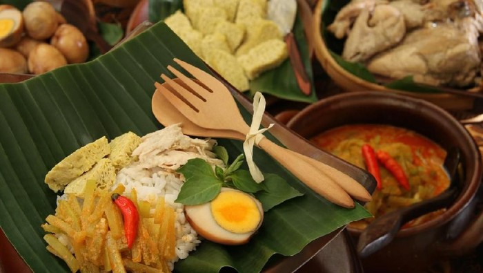 Nasi Liwet Solo, the popular traditional rice dish from Solo / Surakarta. It consists of fragrant, savory rice cooked in coconut milk and served with side dishes of pulled chicken cooked in white curry, coconut gravy, marble eggs, chayote squash in spicy gravy, and egg pudding. The meal is served on traditional earthenware plate lined with banana leaf; then arranged on a dining table that has been covered with Javanese batik table cloth. The individual meal served is in the selective focus zone, leaving all other side dishes on the table in blur.