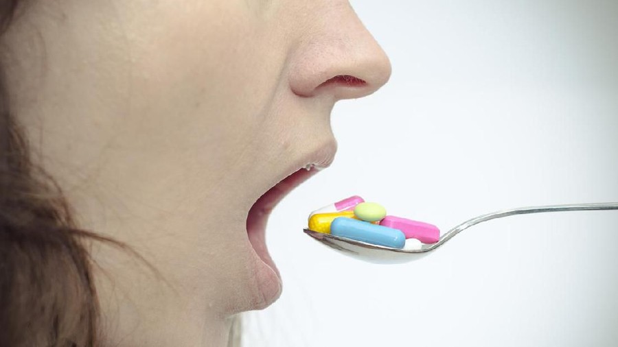 A woman opens her mouth for lots of colorful pills on a spoon.