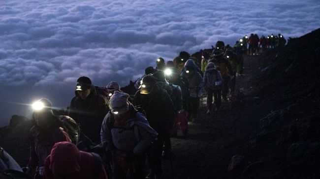 A group of hikers climb to the top of Mount Fuji just before sunrise as clouds hang below the summit Tuesday, Aug. 27, 2019, in Japan. (AP Photo/Jae C. Hong)