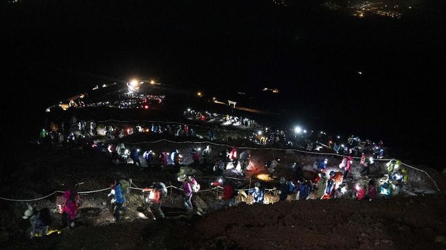 Matahari oranye dan "ombak" awan menjadi incaran pendaki pagi buta di Gunung Fuji.