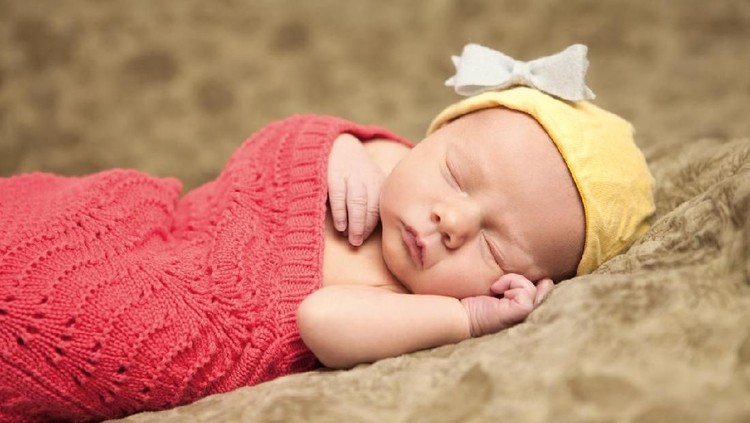 Baby girl Portrait of a newborn baby with yellow hat and white bow, wrapped in red knit blanket.