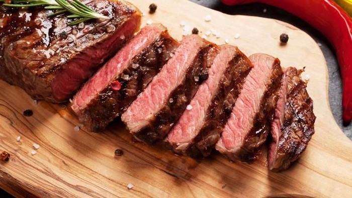 Grilled striploin sliced steak on cutting board over stone table