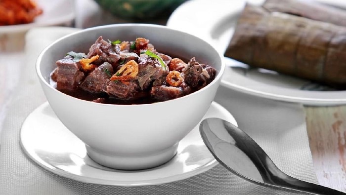 portrait of a bowl of coto makassar served with burasa