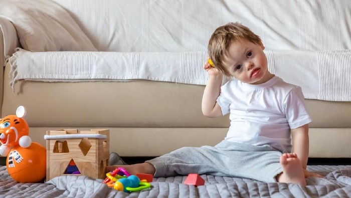 Cute small boy with Down syndrome playing with toy in home living room