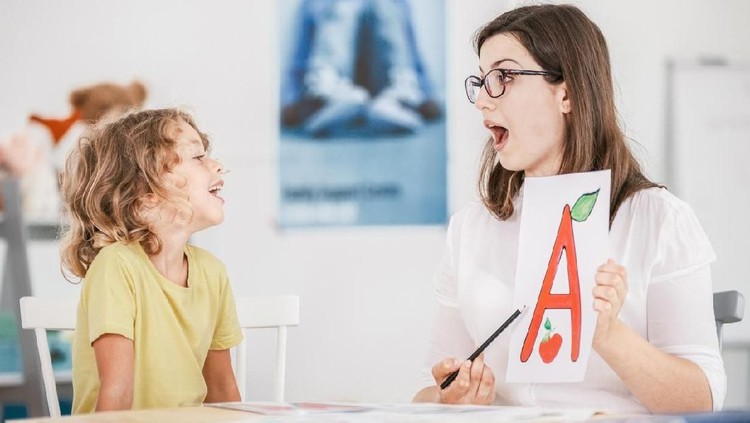 Speech therapist working with a child on a correct pronunciation using a prop with a letter 'a' picture.