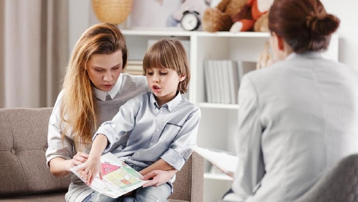 Speech therapist working with a child on a correct pronunciation using a prop with a letter 'a' picture.
