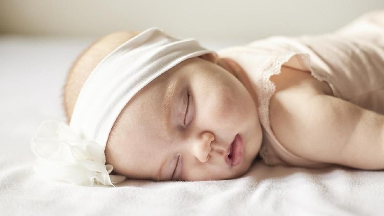 Cute little baby girl slepping with white bow flower on her head