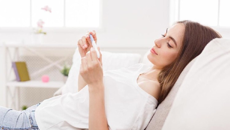 Happy woman holding pregnancy test, beautiful young female at home lying down on sofa. Copy space. Family, child expectation and maternity concept