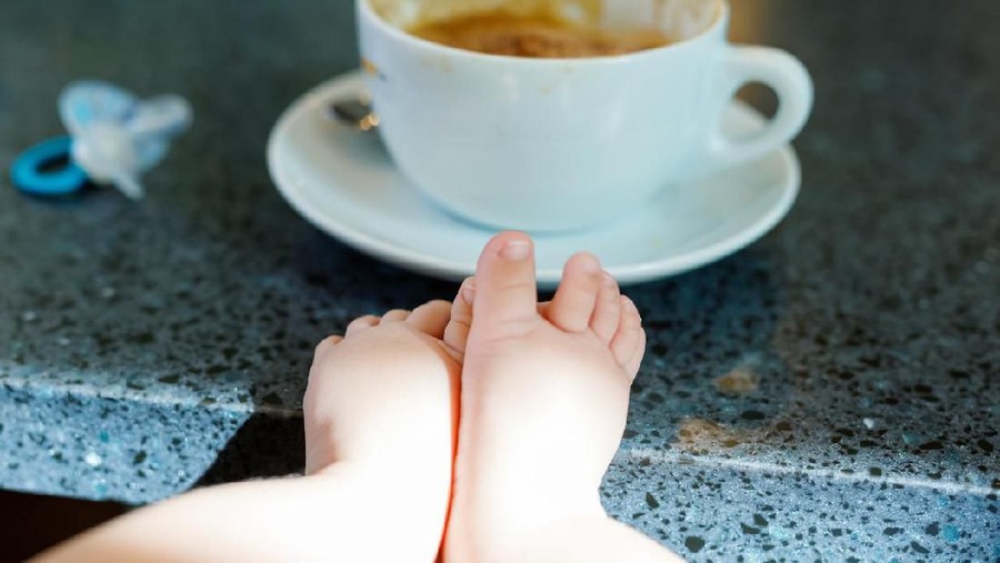 Cup of coffee and baby feet. Concept of working mother and newborn baby. Woman and mum as student.