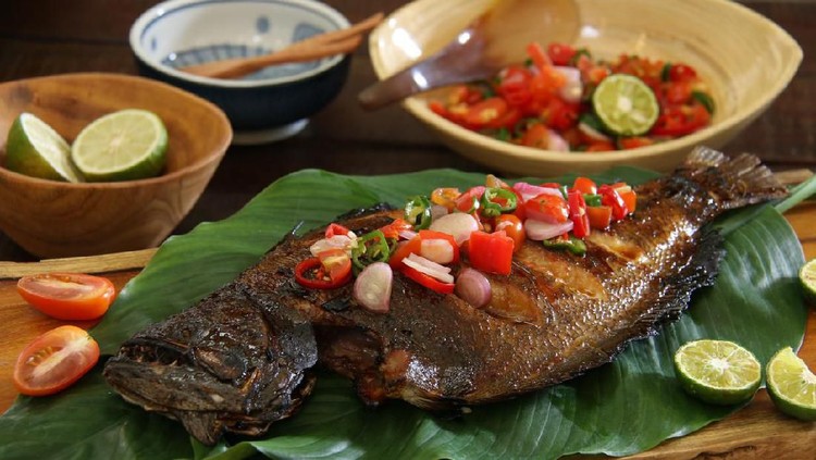 gurame Ikan Bakar Dabu-Dabu, the popular grilled fish dish from Manado, North Sulawesi. The fish is lightly seasoned then grilled; served with the spicy tomato salsa. The fish is plated on a wooden serving block lined with layers of broad green leaves. Accompanied with extra salsa and limes.
