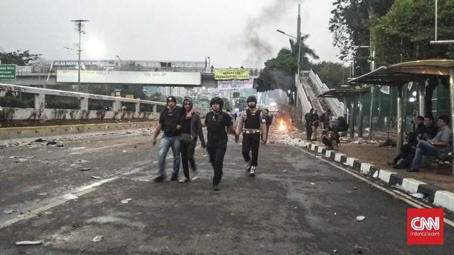 Polisi berompi dengan tulisan Polda Metro Jaya terlihat mengamankan setidaknya dua orang usai berhasil memukul mundur mahasiswa aksi dari depan Gedung DPR.