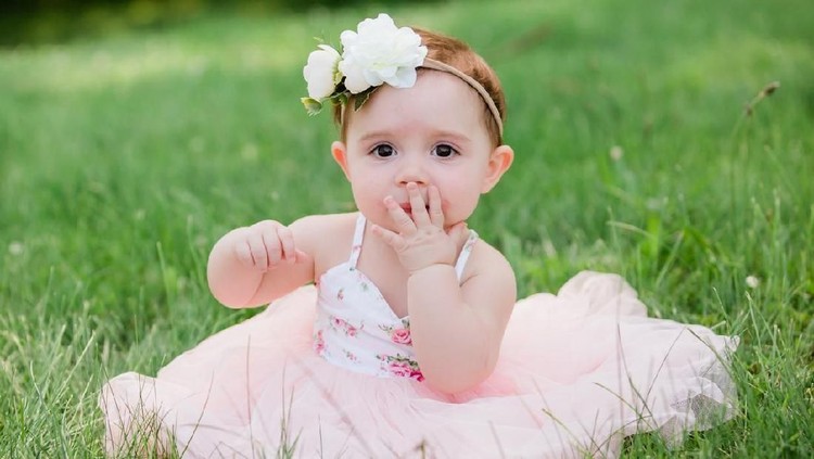 Cute one year old caucasian girl outside in grass wearing a pink summer dress and floral headband
