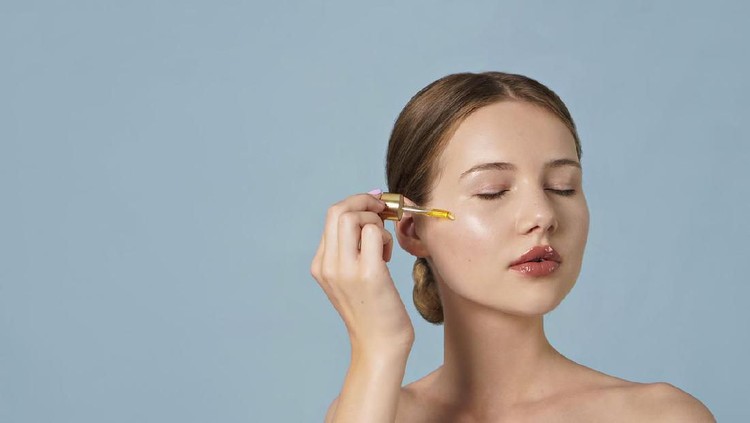 portrait of young woman applying serum on her face on blue background