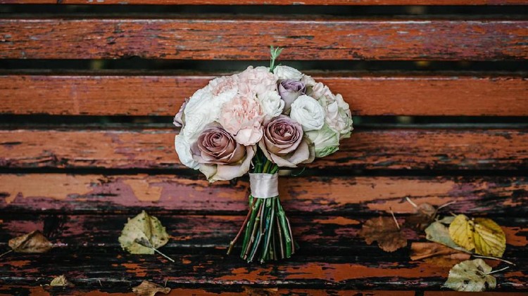 The wedding bouquet of the bride is on a bench with yellow autumn leaves in the park. Bouquet of pale pink, white and brown flowers.