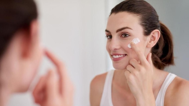 Shot of an attractive young woman applying moisturiser in front of a bathroom mirror
