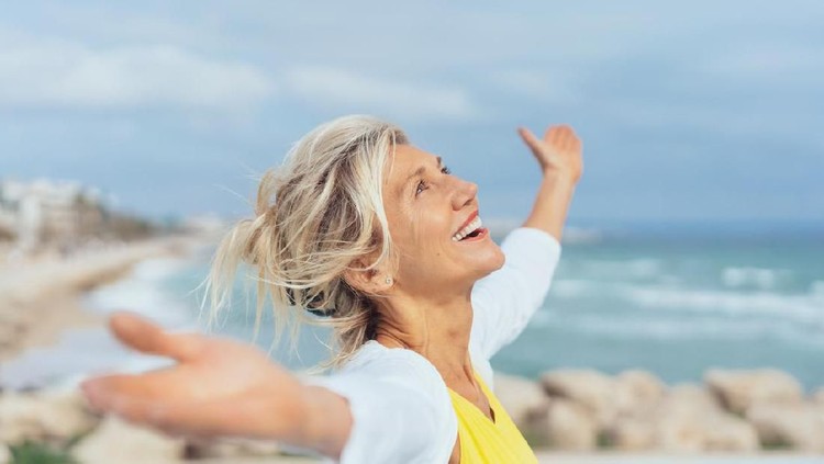Joyful woman enjoying the freedom of the beach standing with open arms and a happy smile looking up towards the sky