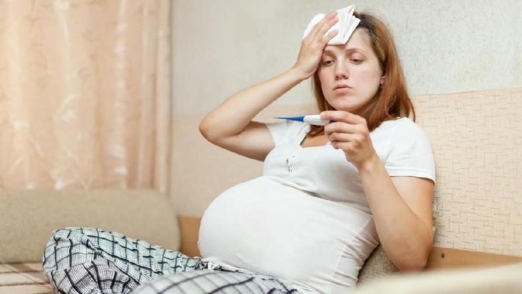 pregnant woman sitting on sofa with thermometer in living room