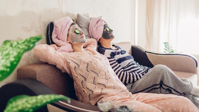 Mother and her adult daughter relaxing with facial masks and cucumbers applied. Women chilling and having fun at home sitting on couch