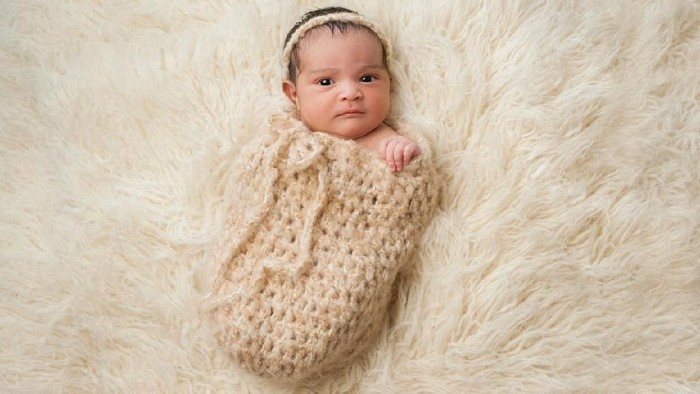 One month old baby girl swaddled in a beige wrap. Shot in the studio on a white blanket.