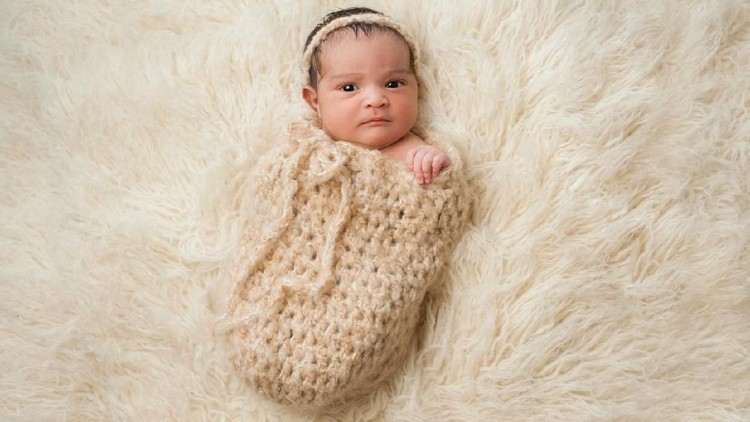 One month old baby girl swaddled in a beige wrap. Shot in the studio on a white blanket.