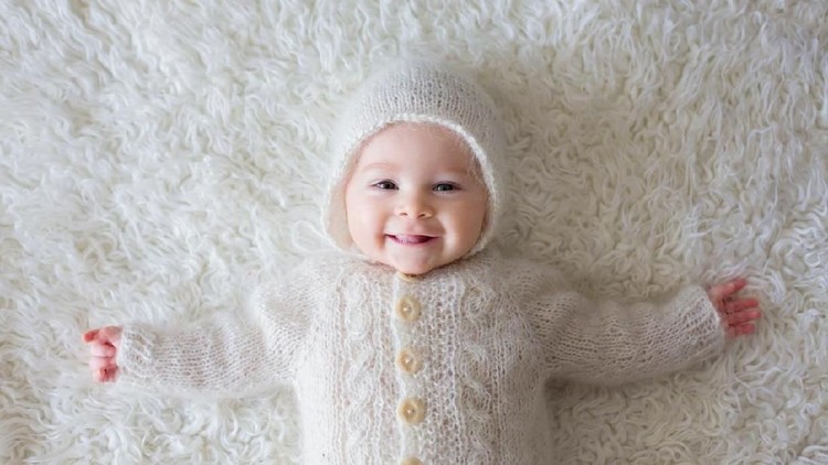 Close portrait of a little baby boy in white knitted onesie and a hat, smiling