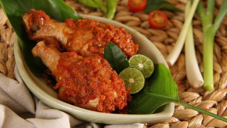 Ayam Rica Rica Ayam Rica-Rica, the popular and traditional dish from Manado, chicken braised in spicy red chili paste. Two drumsticks are arranged on a small ceramic plate that has been lined with a banana leaf. Two lime halves and a lime leaf are used to garnish the dish. The plate is placed on a woven bamboo place mat. Some of the herbs and spices are also placed on the place mat.
