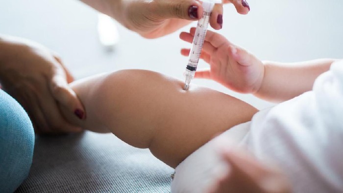 A latin woman injecting medicine on baby's thigh in a horizontal low section shot indoors.