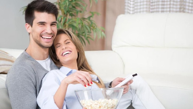 zodiak Couple watching TV, eating popcorn on a sofa at home