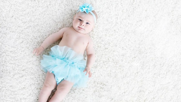 Adorable baby girl on white background wearing turquoise tutu skirt. Cute little child laughing and smiling. Happy carefree baby. Childhood, new life concept.