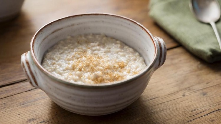 Photograph of a rustic hand made bowl filled with freshly made Porridge, topped with sprinkled Demerara sugar. Photographed on a rustic old pine rustic table.