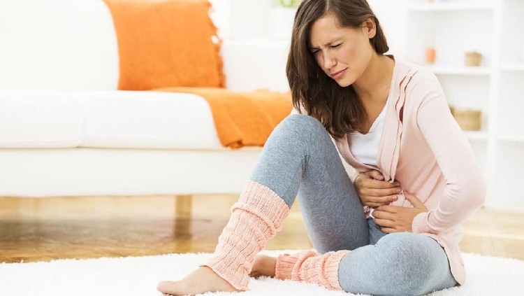 956151356 Shot of unhealthy young woman with stomachache leaning on the bed at home.