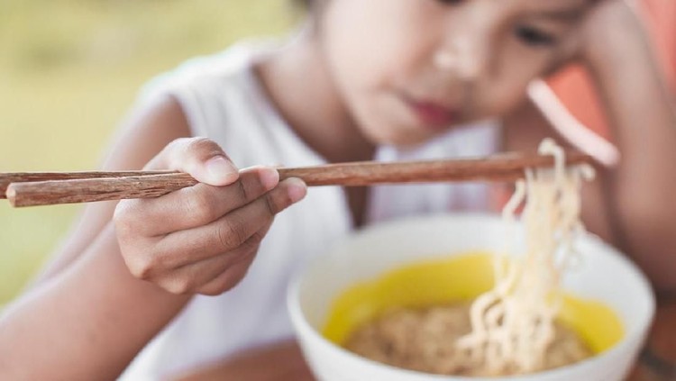 Cute asian child girl eating delicious instant noodles with fork in the nature background